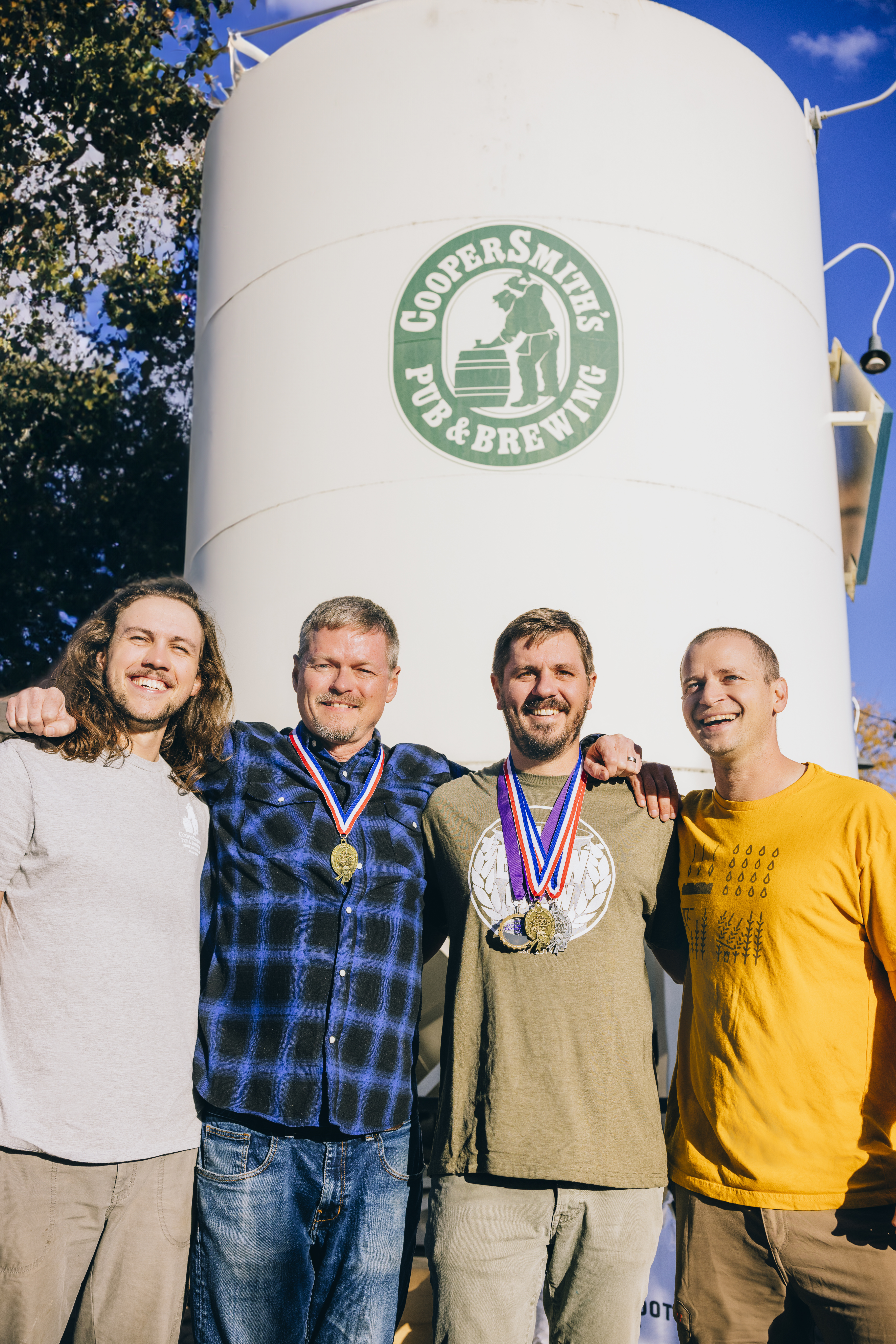 CooperSmith's brewing team standing in front of the CooperSmith's beer storage tank wearing their gold medals.
