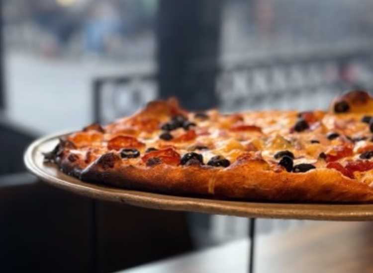 Untitled design (4) Several people reach for slices of coopersmiths-pizza on a metal tray at a restaurant table, creating a sense of sharing and togetherness.
